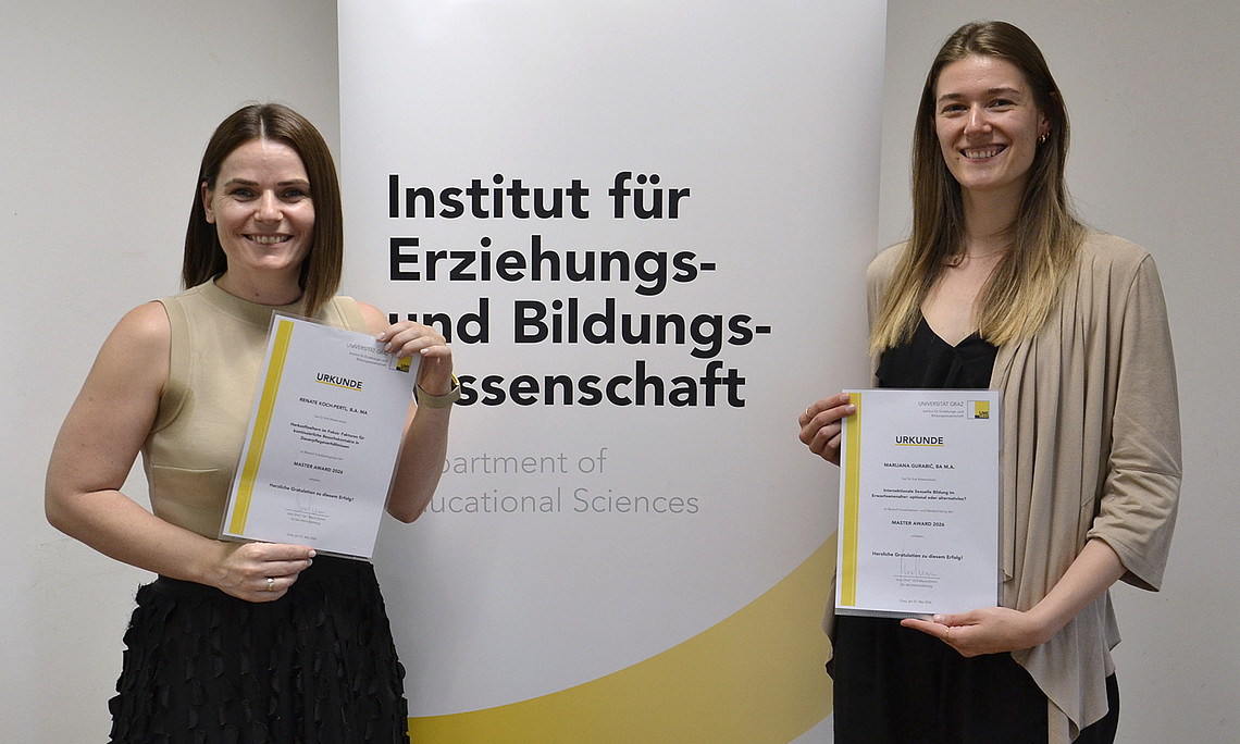 zwei junge Frauen, die vor einem Rollup stehen und Urkunden halten