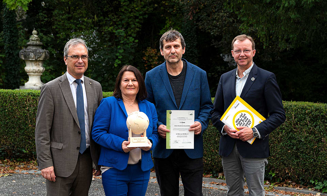 Der „Green Academia Award“ der Uni Graz ging heuer an die Erziehungswissenschaften. Rektor Peter Riedler (links) und Klimaforscher Gottfried Kirchengast (rechts) überreichten die Trophäe aus Holz an Hannelore Reicher und Arno Heimgartner. Foto: Uni Graz/Angele 