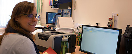 Frau sitzt am Schreibtisch vor einem PC 