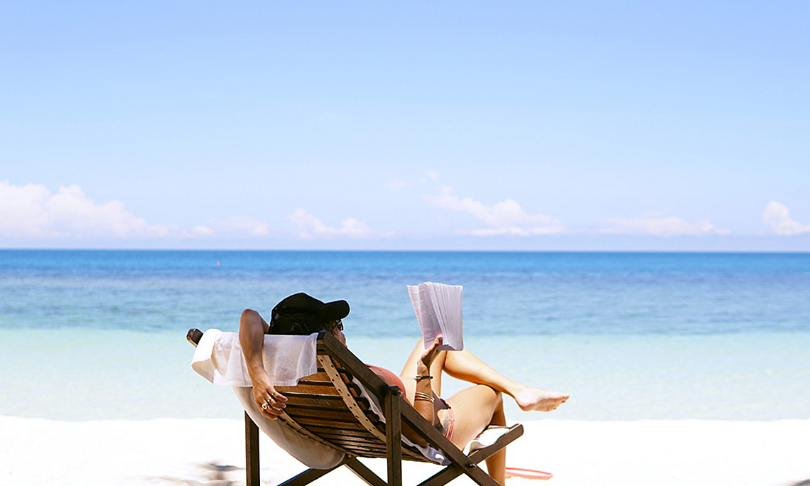 Frau im Liegestuhl am Strand mit Buch in der Hand