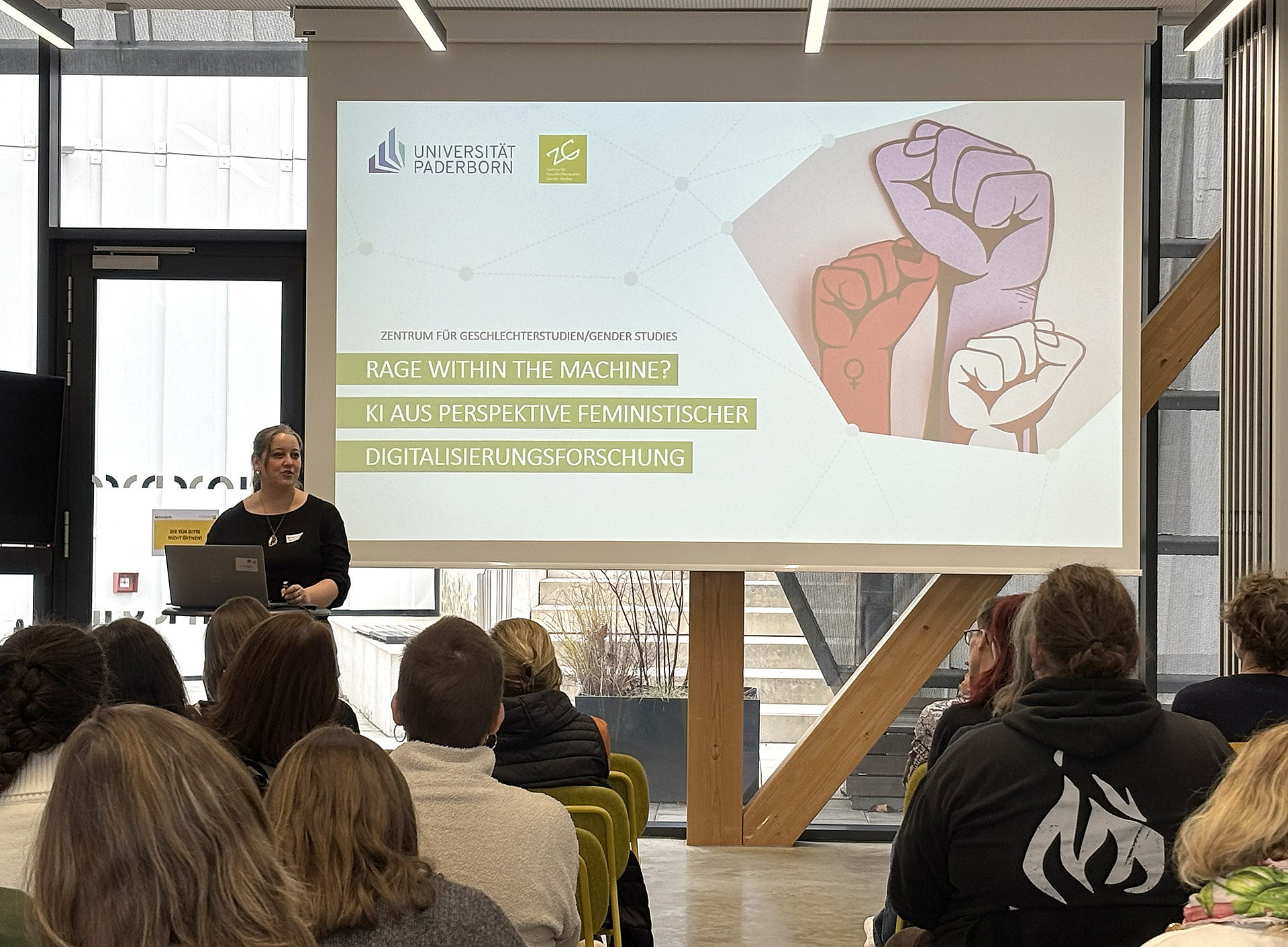 eine Frau steht vor einem Tisch mit Laptop und hält einen Vortrag, hinter ihr sieht man die Leinwand mit der Präsentation. Im Publikum sitzen viele Menschen und hören zu ©Uni Graz/Schmieder