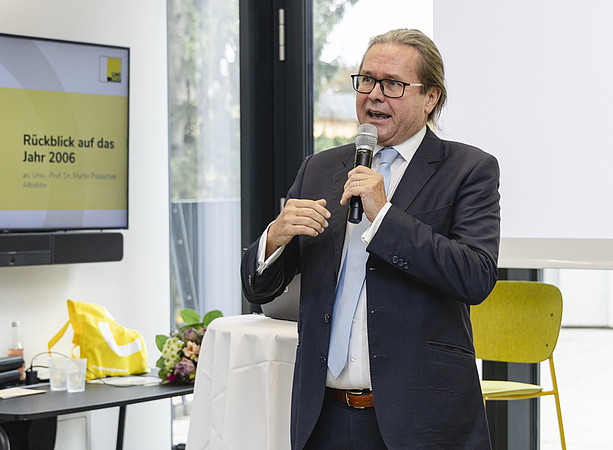 Ein Mann spricht mit Mikrofon vor einer Folie mit dem Titel „Rückblick auf das Jahr 2006“. ©@foto-gasser.at