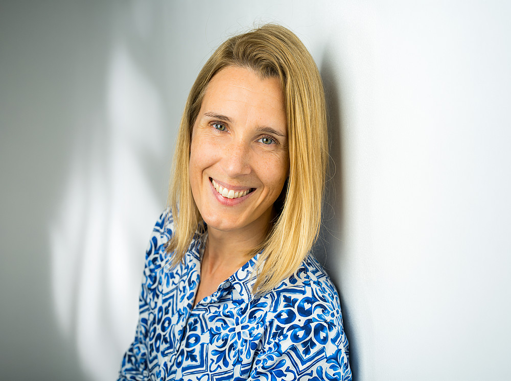 Portrait photograph of M. Jandrisits wearing a blue patterned blouse against a light-coloured background ©Opernfoto