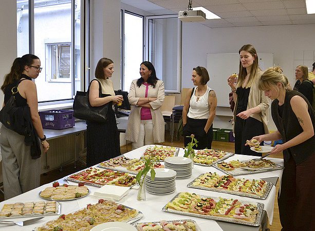 eine Gruppe an Menschen steht um ein Buffet herum; ein paar essen Brötchen, ein paar unterhalten sich ©Uni Graz/Braunegger