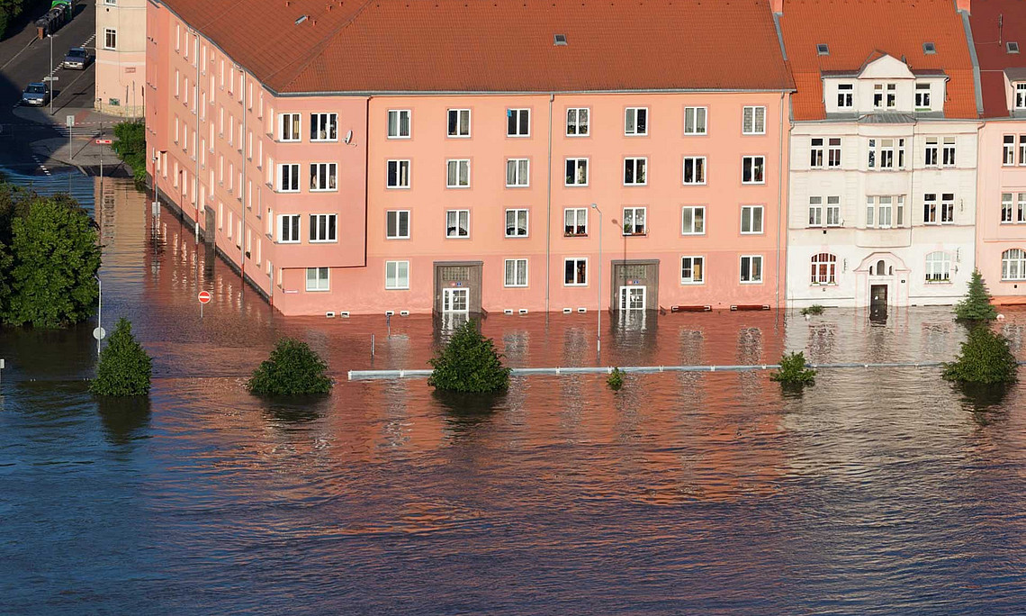 Altbauten-Häuserblock einer Stadt, Hochwasser, Bäume an der Straße mit den Stämmen im Wasser