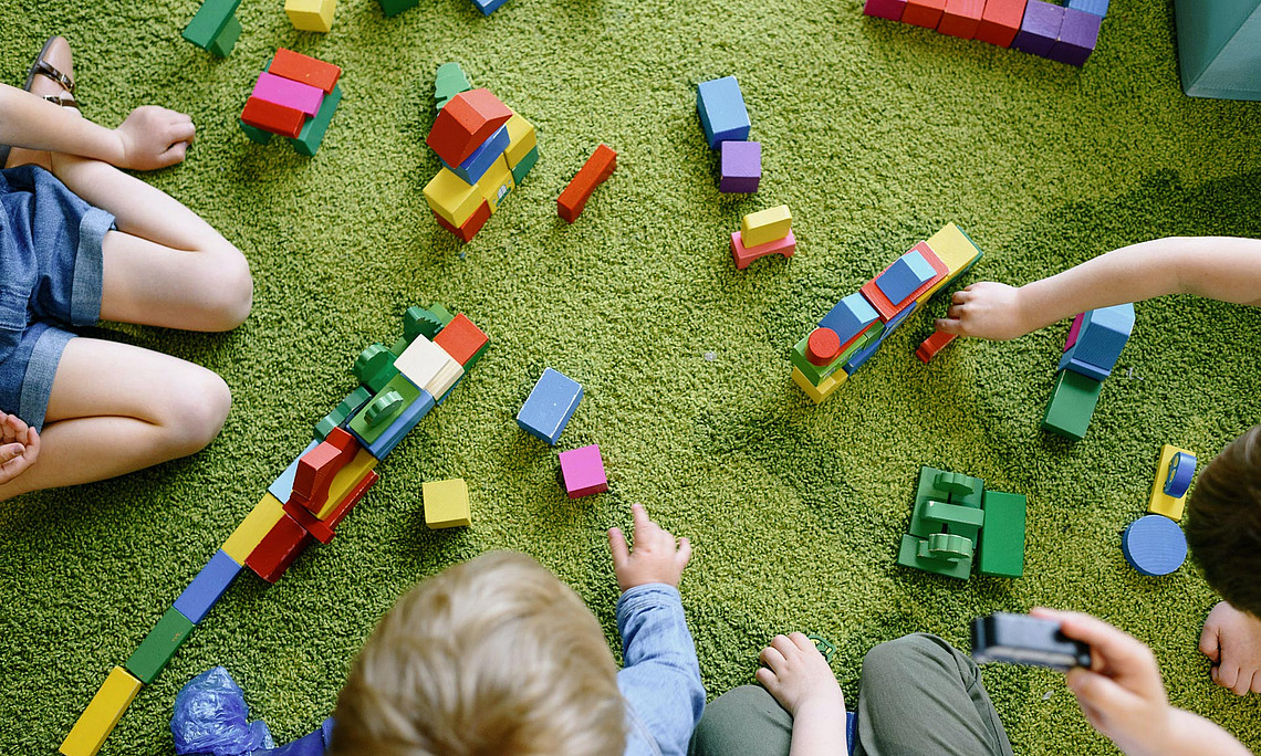Kinder spielen mit Holzspielzeug auf dem Boden.