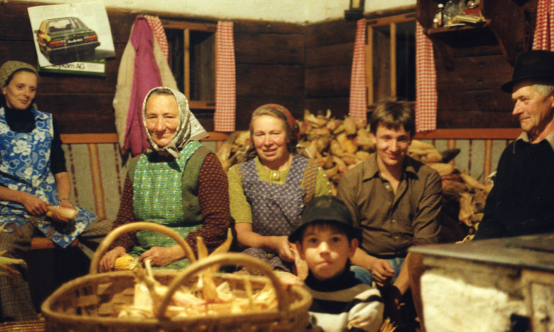 A farming family, six people from three generations, in a parlour with a basket full of unpeeled corn cobs.