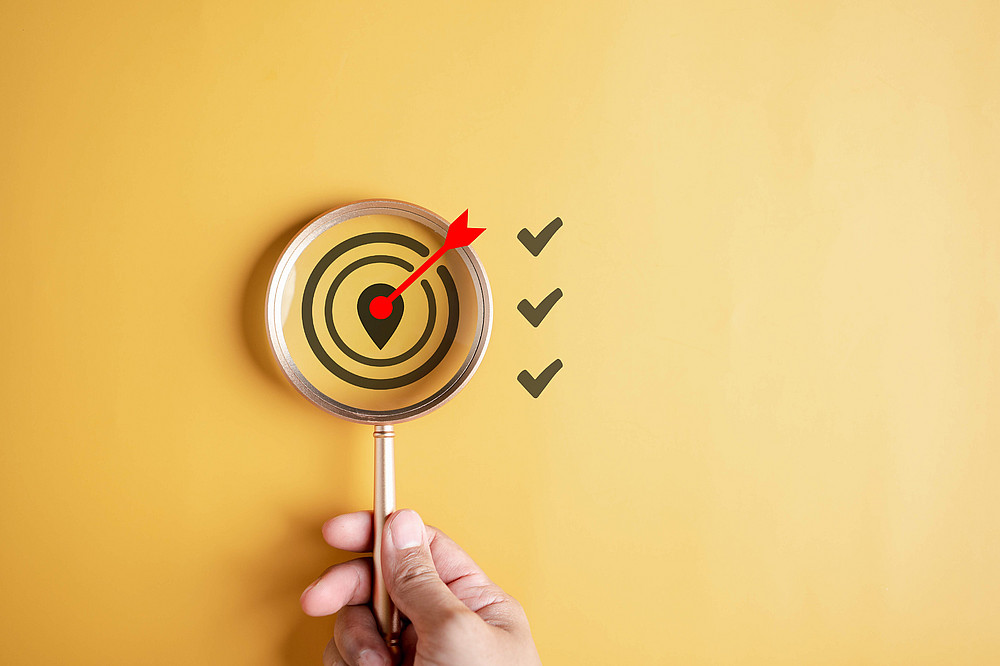 Magnifying glass on a yellow background, held by a hand. There are three checkboxes on the right. This photo symbolizes the topic of behavioral suggestions and duties. 