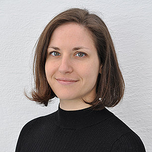 Portrait einer jungen Frau mit schulterlangen braunen Haaren und grünen Augen in einem schwarzen Rollkragenpullover