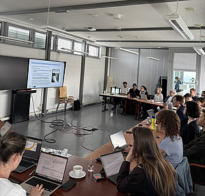 Rund 15 Erwachsene sitzen mit Laptops an Tischen und verfolgen eine Präsentation auf einem Bildschirm mit Folien zur österreichischen Klimawandelanpassungsstrategie. ©Paul Schweighofer