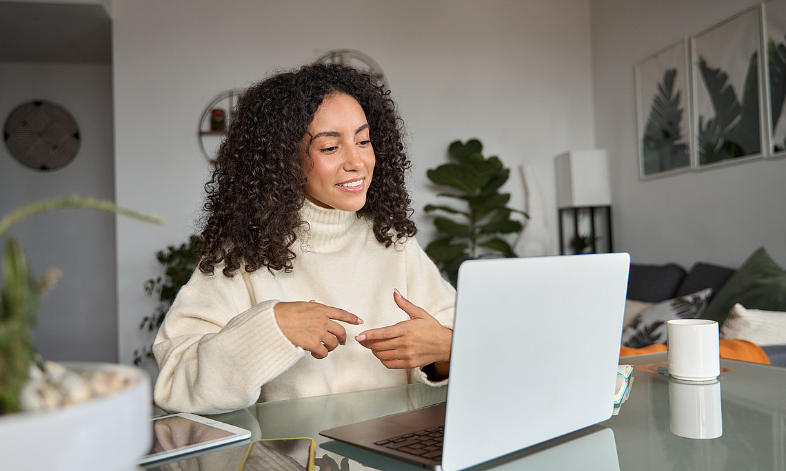 Young woman sitting in front of her laptop in her apartment and taking part in an online meeting.