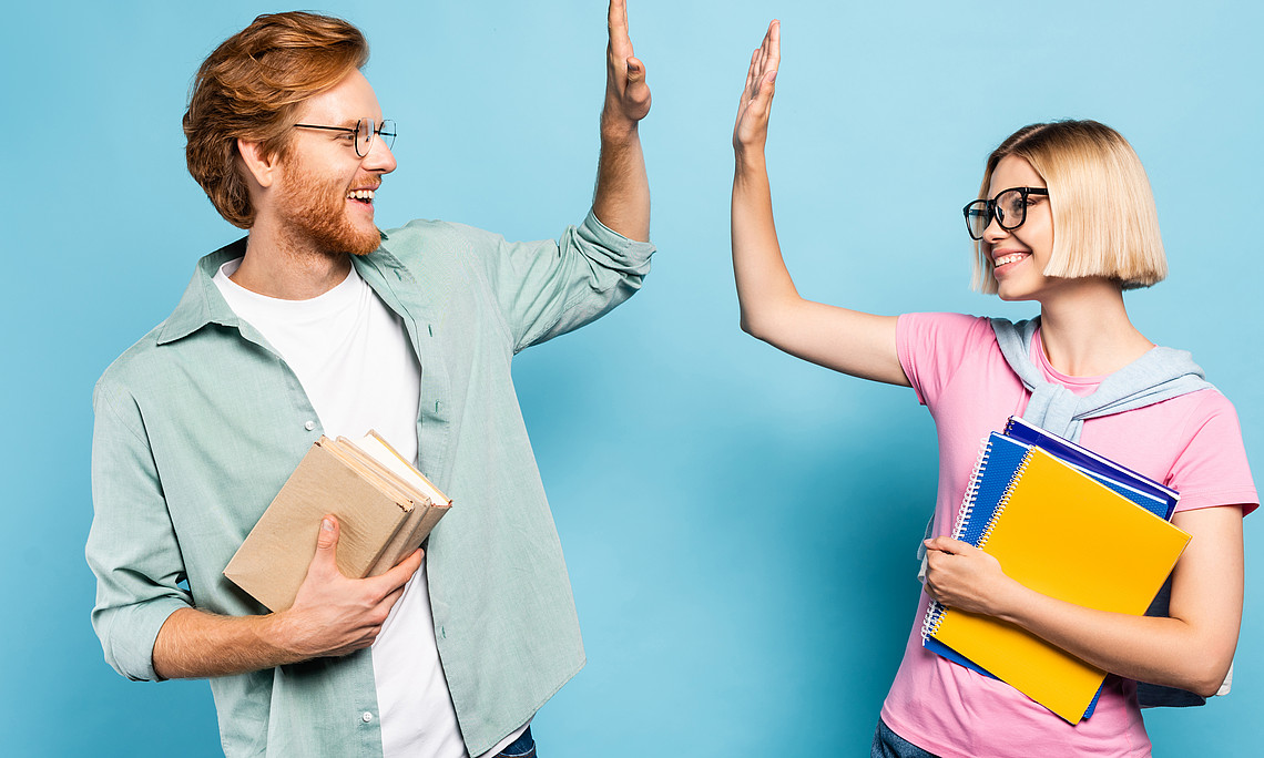 Zwei junge Studierende mit Notebook und Büchern geben sich High Five