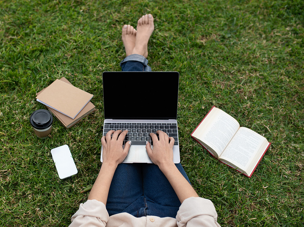 student sitting on grass with laptop typing ©By Prostock-studio; stock.adobe.com 