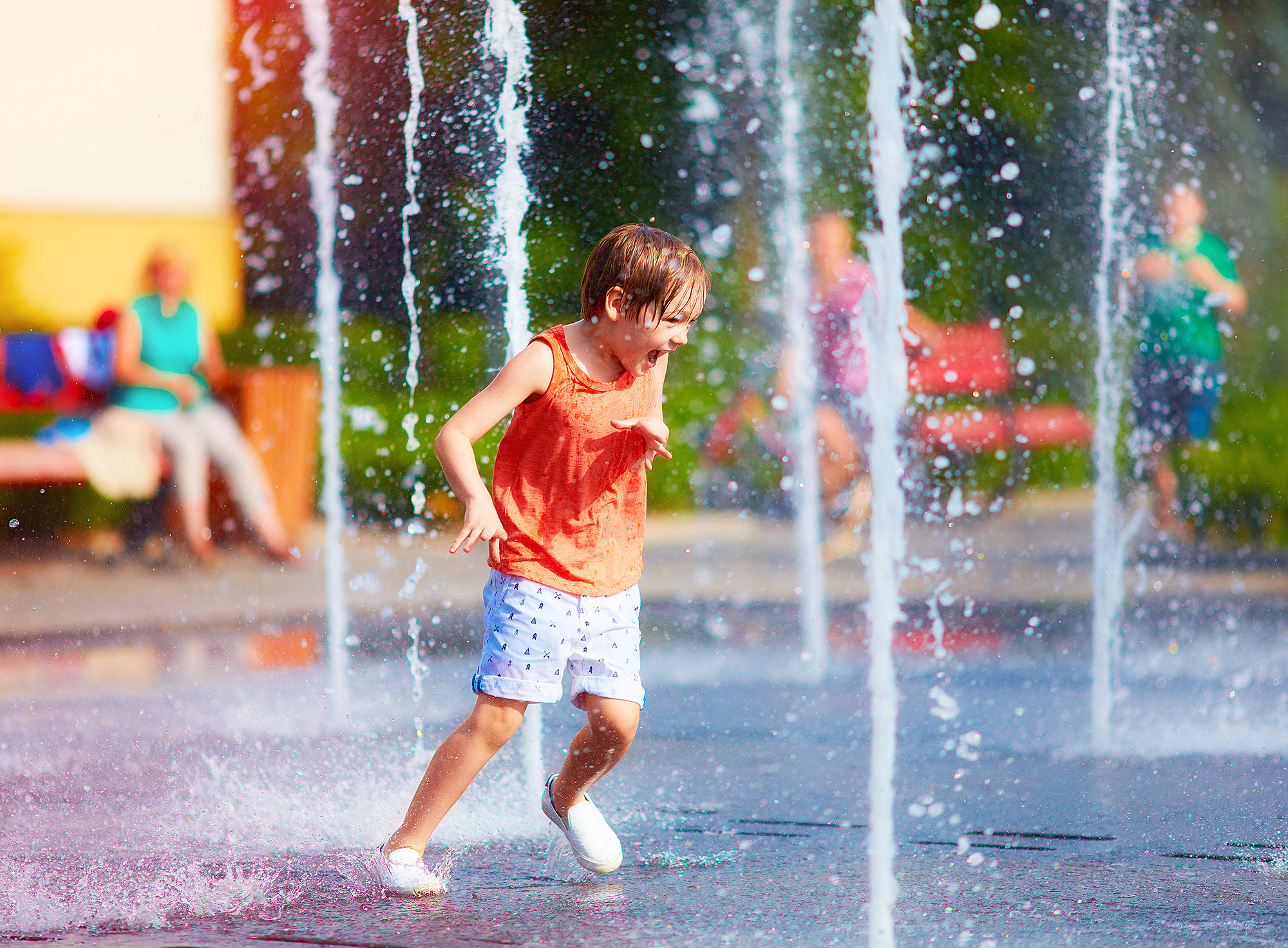 excited boy having fun between water jets, in fountain. Summer in the city 