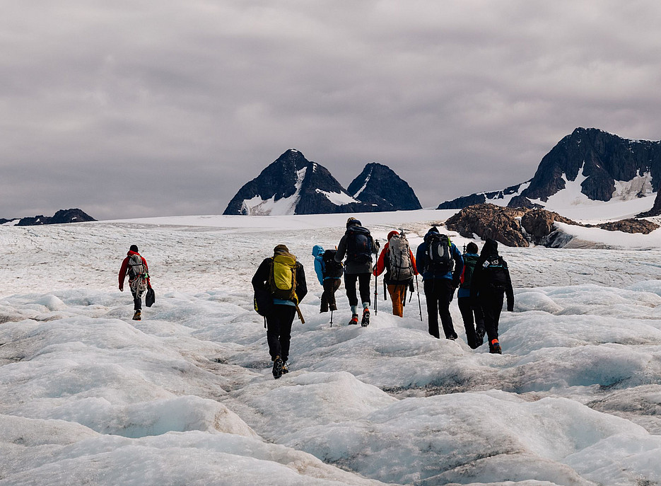 Eine Gruppe mit wandernden Menschen läuft über die eisige Oberfläche von Gletschern in Grönland. Das Eis schmilzt und im Hintergrund sind Berge zu sehen. ©Karl Steinegger