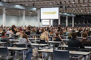 A hall full of young people sitting at tables taking an exam
