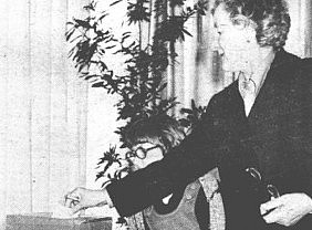 The picture shows a person placing a piece of paper into a box labeled "ZA." A child wearing glasses and a sweater stands nearby, observing the action. ©@ Naš čas, 18. April 1980.