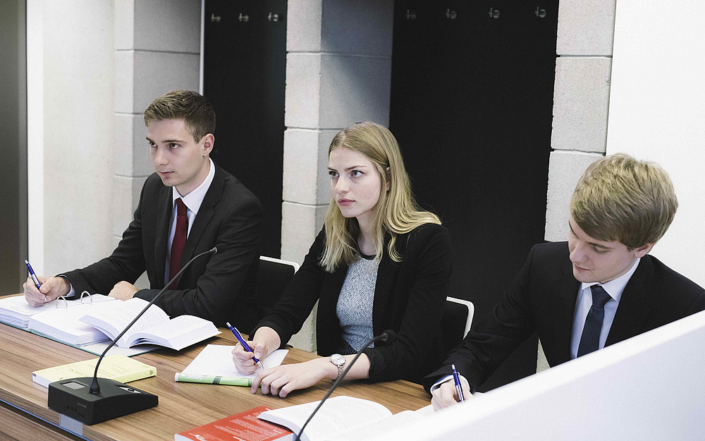 Subject photo for the course "Criminal Procedure in Practice", three students sitting at the table at the Moot Court in the Negotiation Hall of the University of Graz ©Uni Graz/Kanizaj