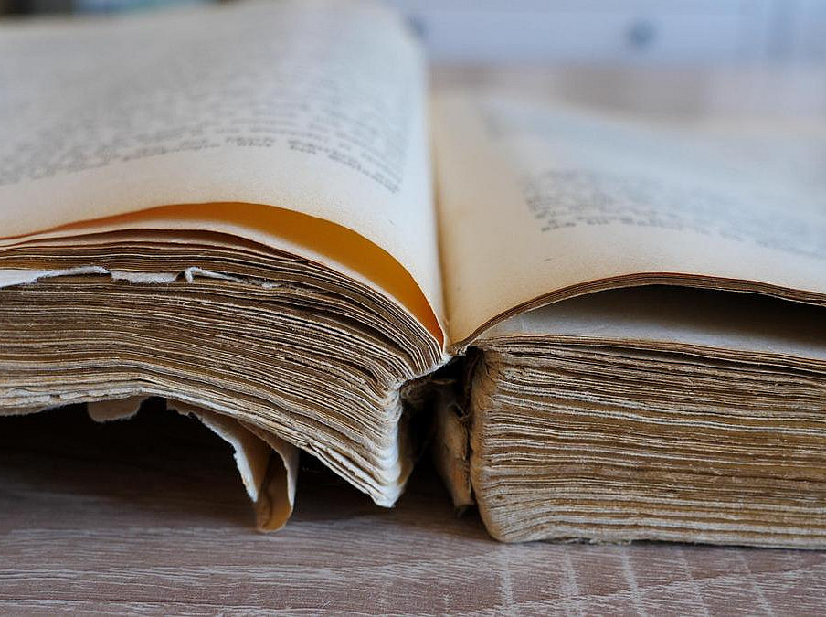 Ein großes, altes Buch mit vergilbtem Papier und abgestoßenen Kanten liegt aufgeschlagen auf einem Tisch. ©stock.adobe.com / zelwanka 