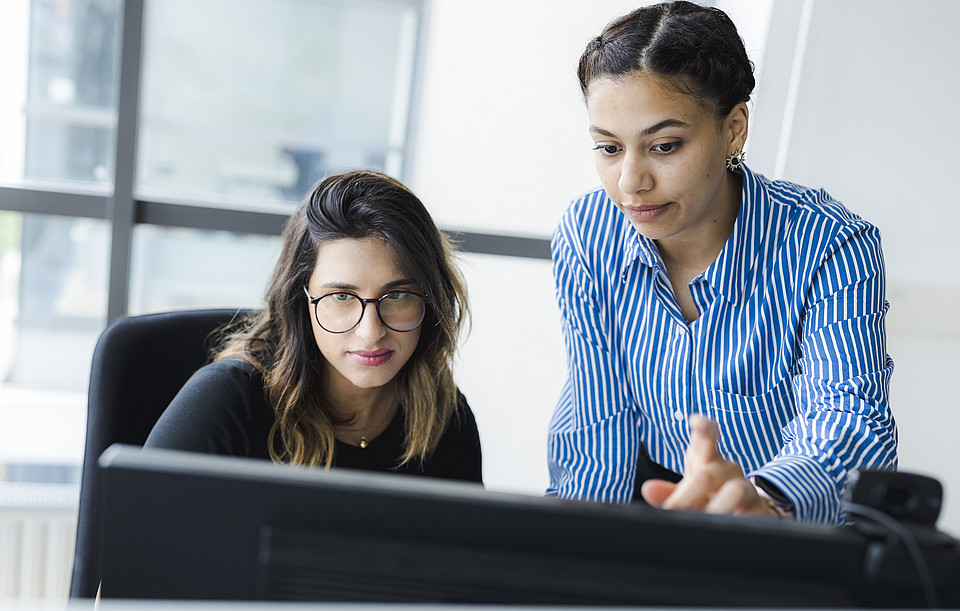 2 Personen vor Computer, arbeiten zusammen