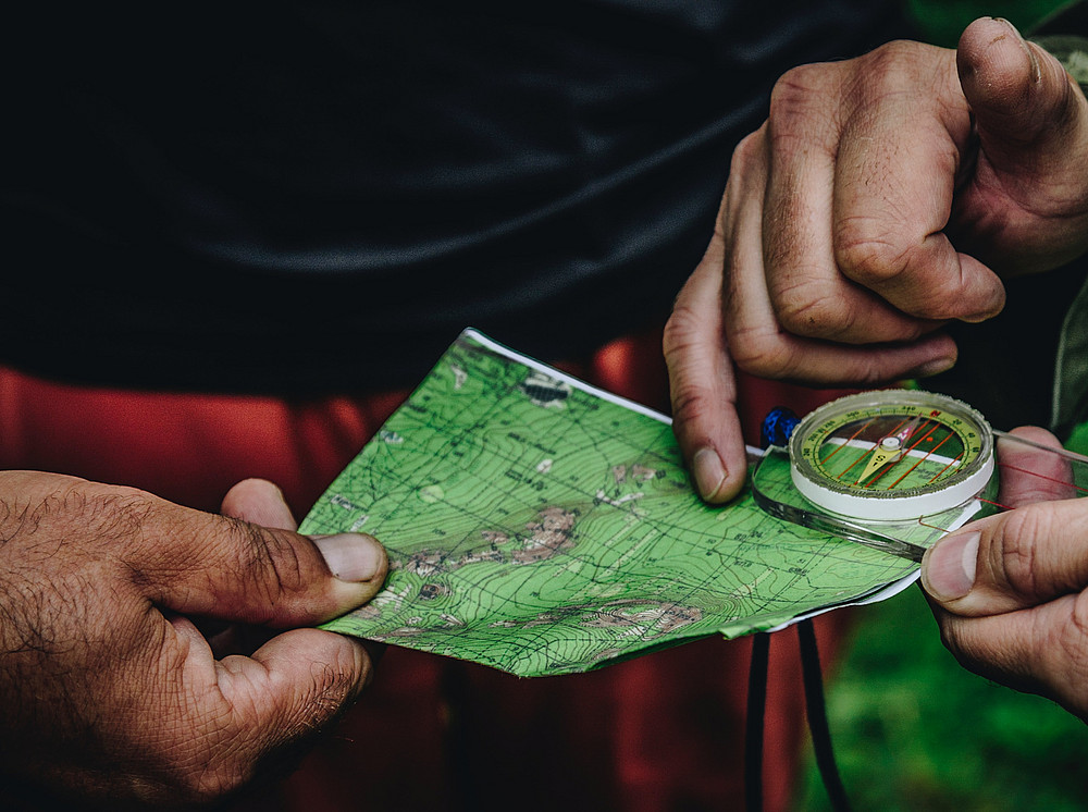 Nahaufnahme von zwei Paar Händen, die eine Landkarte und einen Kompass in den Händen halten und nach dem Weg suchen ©Photo by Daniil Silantev on Unsplash