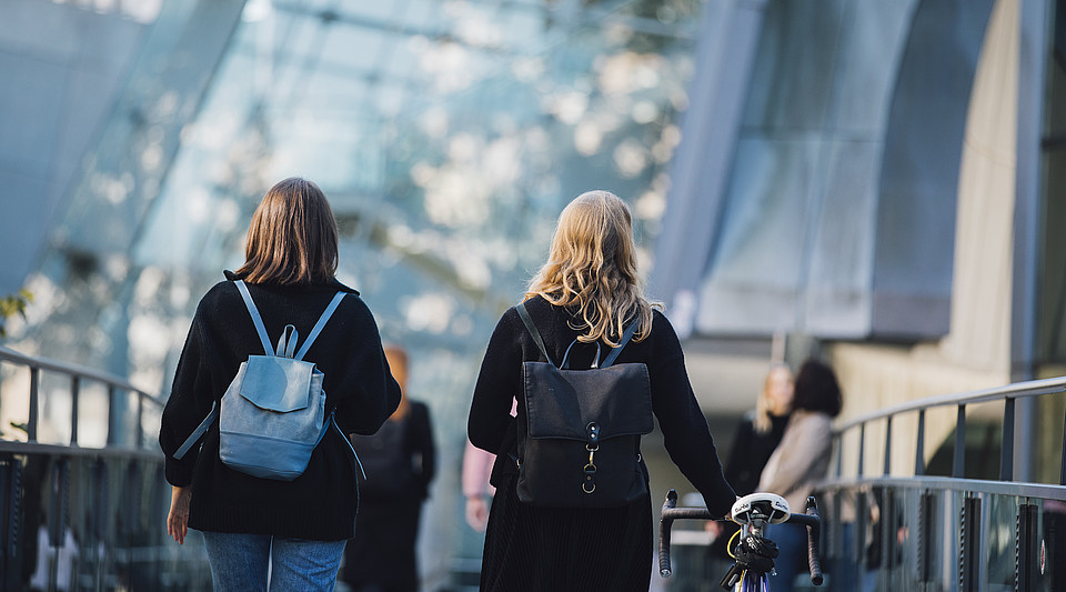 Zwei Studierende - mit dem Rücken zur Kamera - flanieren über den Campus