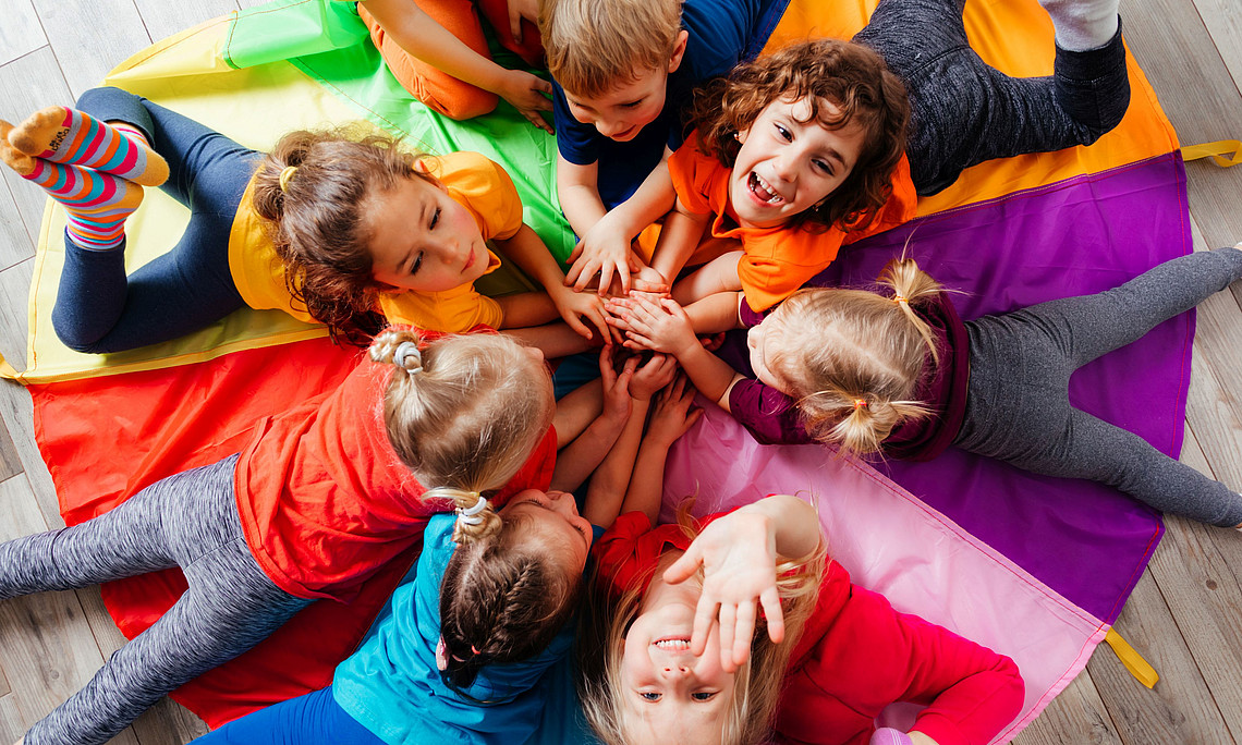 Mehrere Kinder spielen liegend auf runder Decke