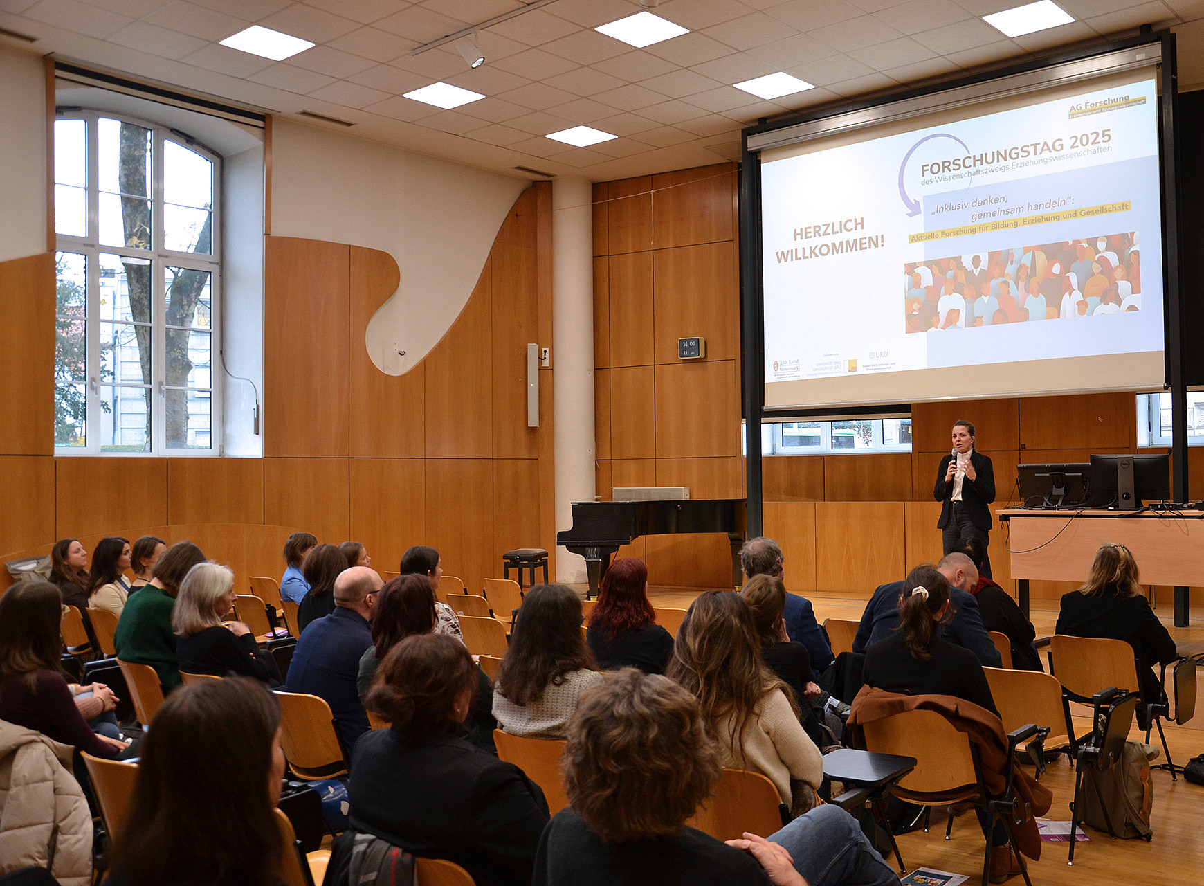 eine Frau im Anzug steht in einem Hörsaal auf einem Podium und spricht in ein Mikrofon, im Publikum sitzen viele Menschen und hören zu ©Uni Graz/Braunegger