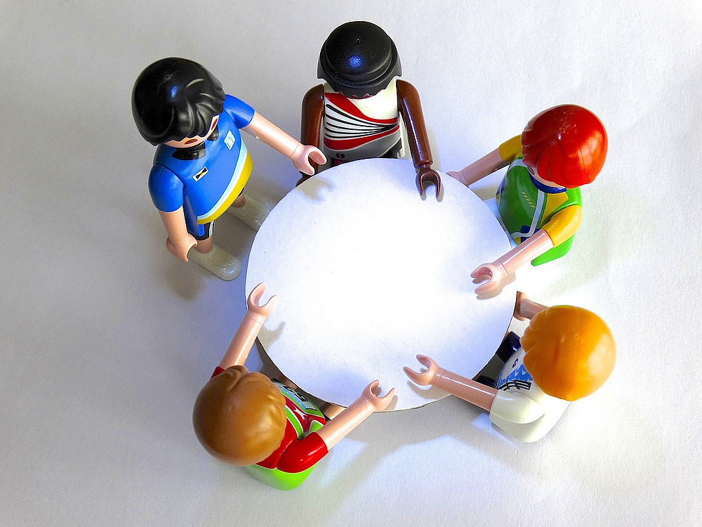 Five Playmobil figures (men and women) stand around a table and it looks as if they are talking to each other animatedly. ©pixabay/pixabay