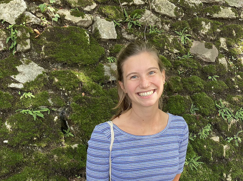 Portrait: Hanna Wäger in front of a moss-covered stone wall 