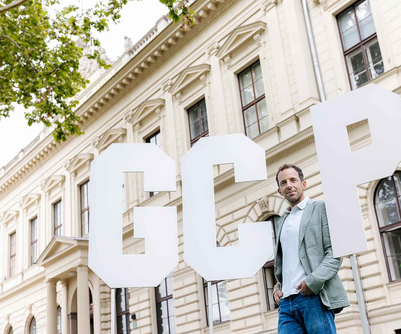 ein Mann steht vor einem historischen Gebäude sowie drei sehr großen Buchstaben G C P