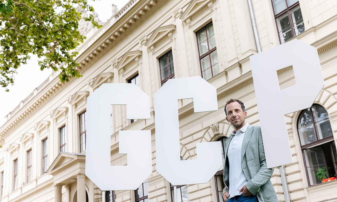 ein Mann steht vor einem historischen Gebäude sowie drei sehr großen Buchstaben G C P