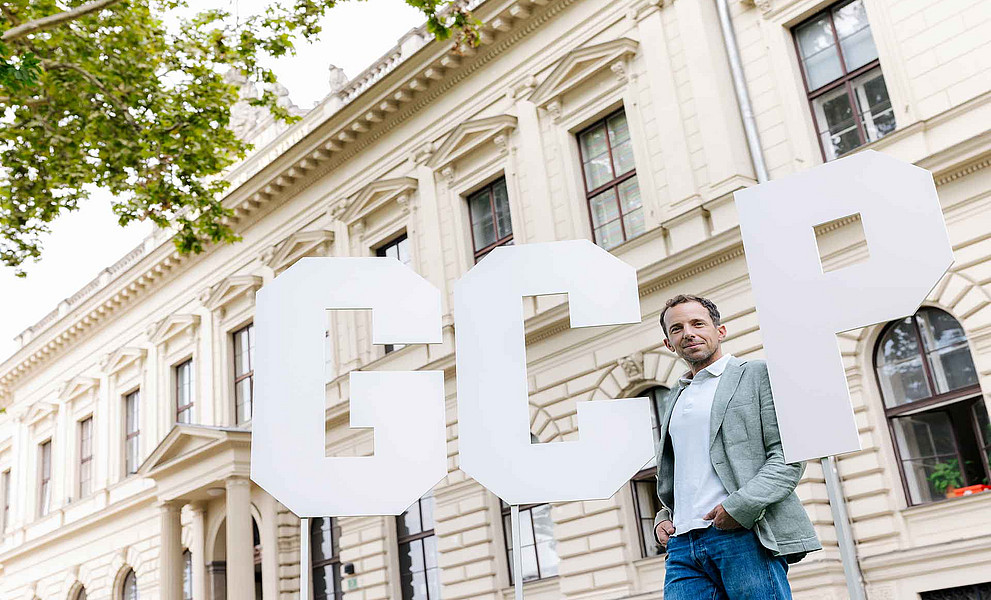 ein Mann steht vor einem historischen Gebäude sowie drei sehr großen Buchstaben G C P
