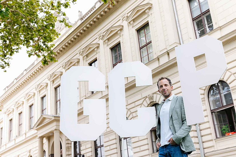 ein Mann steht vor einem historischen Gebäude sowie drei sehr großen Buchstaben G C P