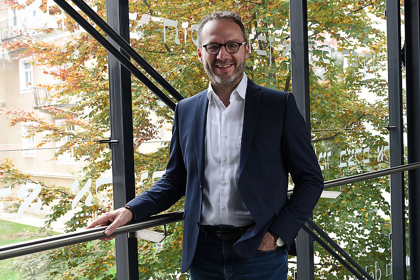 Ralf Lutz in front of a glass wall, behind it a tree with autumn leaves