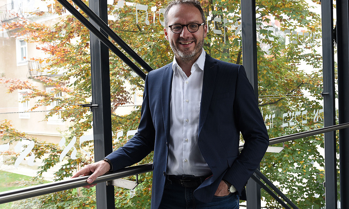 Ralf Lutz in front of a glass wall, behind it a tree with autumn leaves