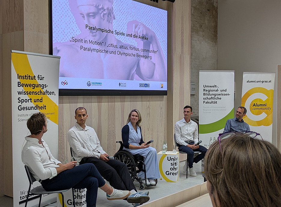 Die vier Vortragenden am Podium mit dem Moderator. Im Hintergrund ein Bildschirm und die Roll-Ups der Universität und Fakultät. ©Mateja Marsel