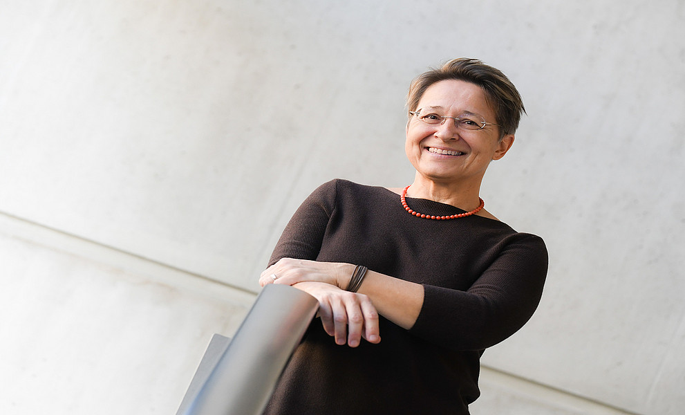 Anita Ziegerhofer, Portrait, vor grauer Betonwand, die Hände auf einem Edelstahl-Geländer