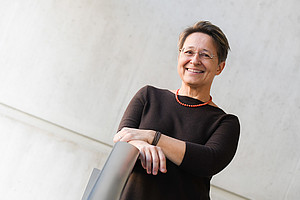 Anita Ziegerhofer, portrait, in front of a grey concrete wall, her hands on a stainless steel railing