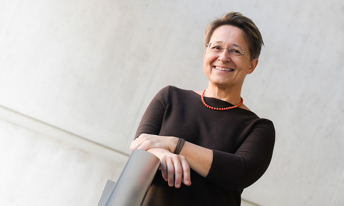 Anita Ziegerhofer, portrait, in front of a grey concrete wall, her hands on a stainless steel railing