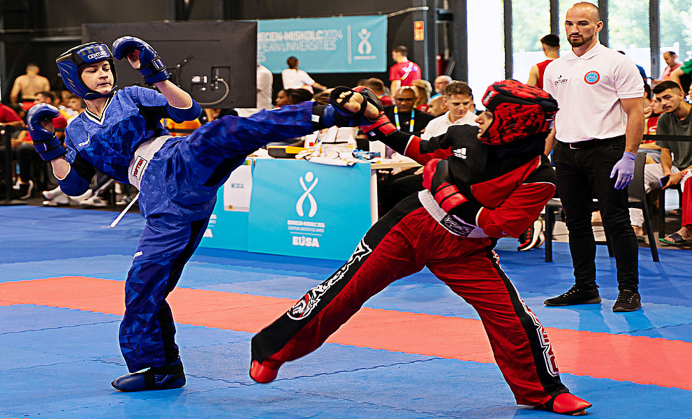 Zwei Kickboxerinnen beim Kämpfen in der Halle, hinten Zusehende und der Schiedsrichter