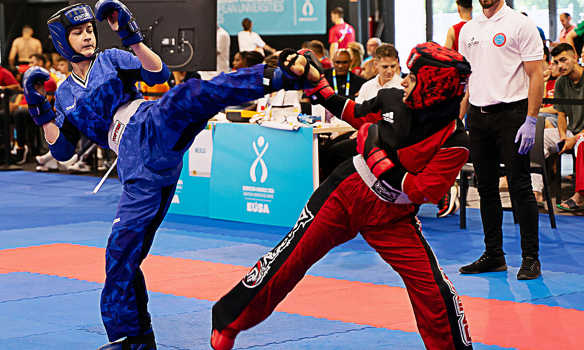 Two kickboxers fighting in the hall, spectators and the referee in the back