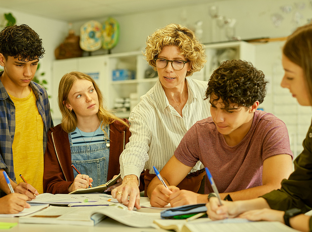 Vier Studierenden wird etwas von der weiblichen Lehrperson gezeigt ©Copyright (c) 2026 Rido/Shutterstock.