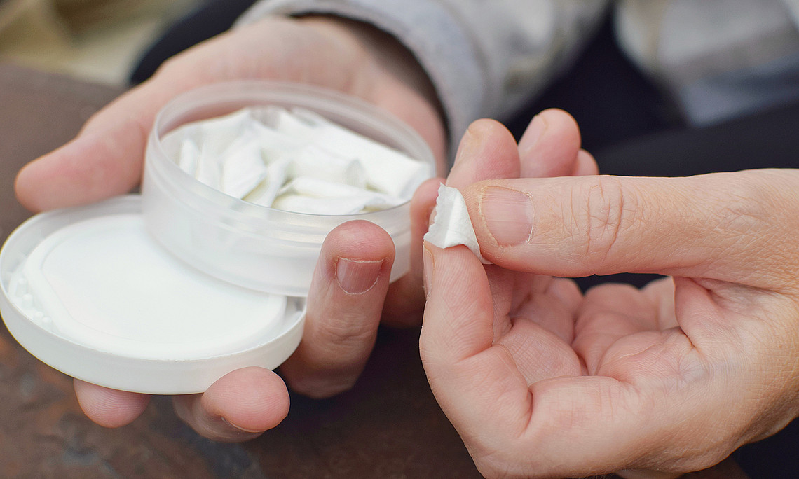 Eine Hand hält eine Dose Nikotinbeutel, die andere nimmt einen davon heraus