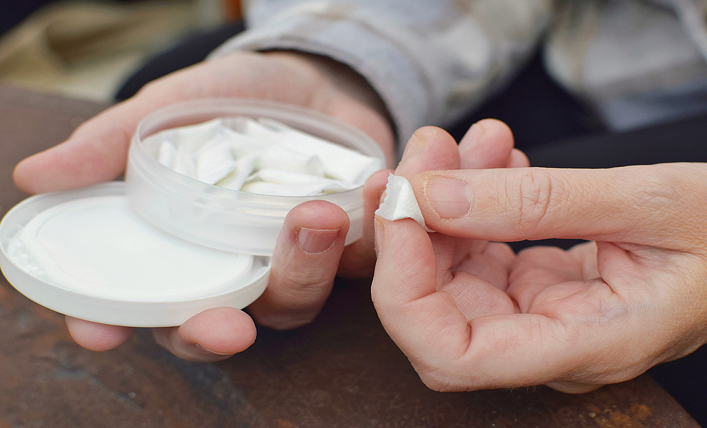 Eine Hand hält eine Dose Nikotinbeutel, die andere nimmt einen davon heraus