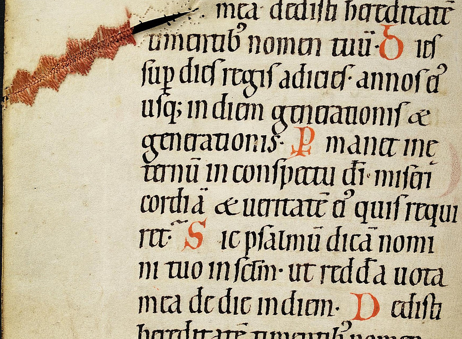 Eine Seite einer mittelalterlichen Handschrift. Auf der linken oberen Seite eine kunstvolle Stickerei 
