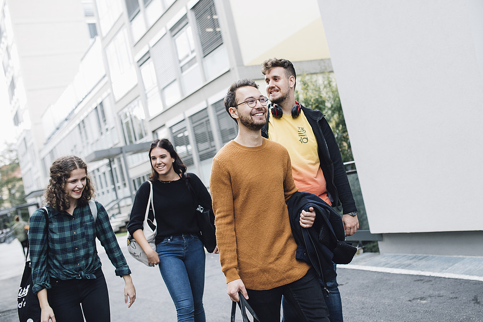 eine Gruppe von Studierenden schlendert über den Campus; sie unterhalten sich miteinander und lachen