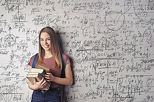Lächelndes Mädchen mit Schulbüchern in der Hand steht vor einer Tafel mit mathematischen Formeln