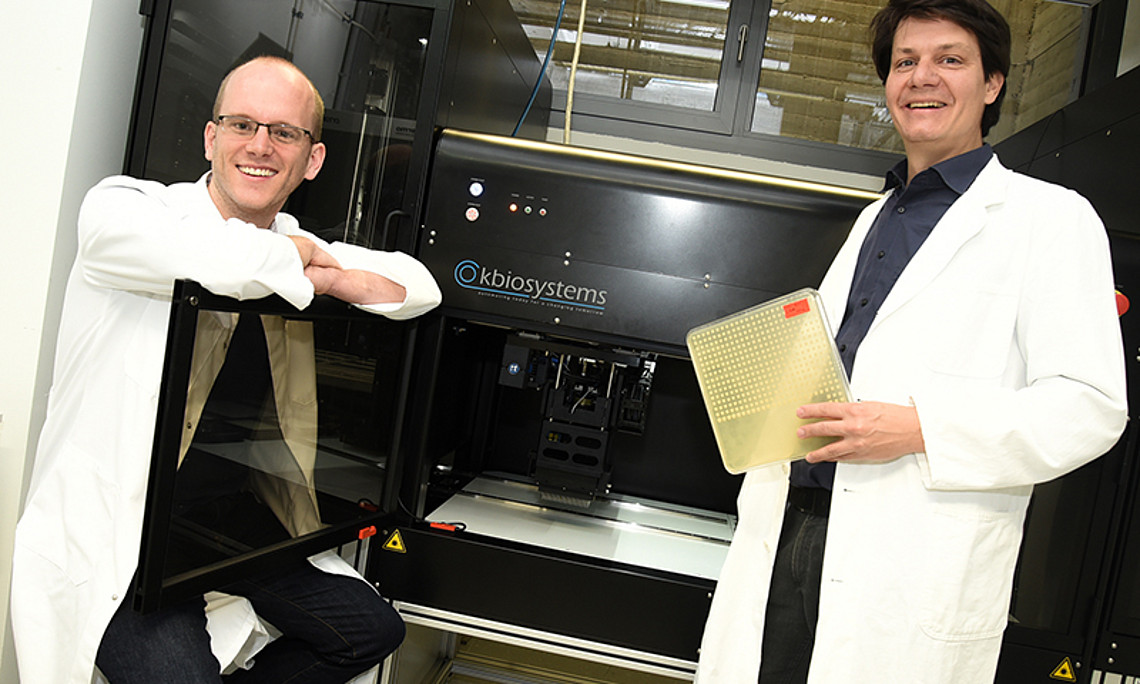 Jonathan Woodsmith (l.) und Ulrich Stelzl (r.) arbeiten mit Bäckerhefe, um große Genbibliotheken mit Hilfe eines Arrayroboters - im Hintergrund - zu durchforsten. 