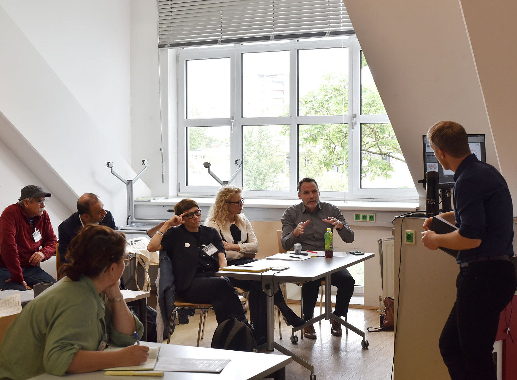 6 Leute sitzen an Tischen in einem Seminarraum und sprechen mit einem Mann, der am Rednerpult steht. ©Uni Graz/Anđela Karać